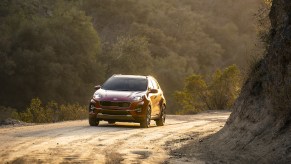 A red 2021 Kia Sportage compact SUV traveling on a dirt road between mountains