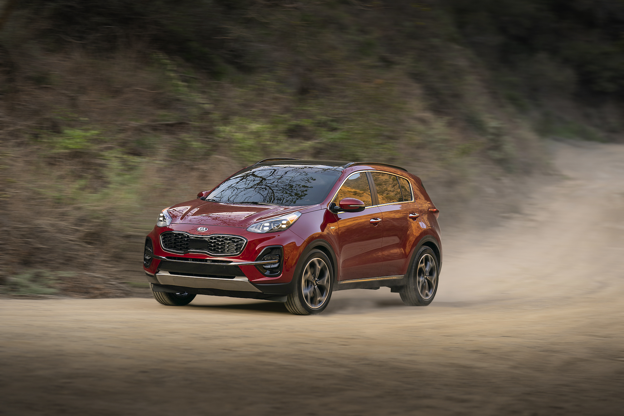 A red 2021 Kia Sportage compact SUV traveling on a dusty mountain road