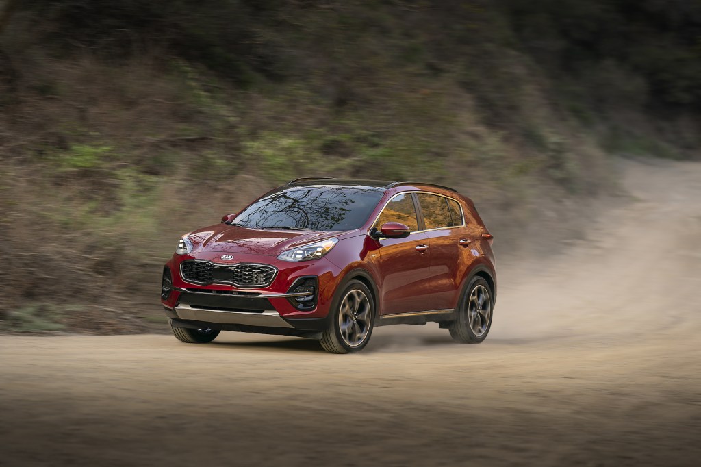 A red 2021 Kia Sportage compact SUV traveling on a dusty mountain road has better resale value than many other crossover models.