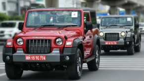 A red 2021 Mahindra Thar driving in front of a gray 2021 Mahindra Thar on an Indian city road