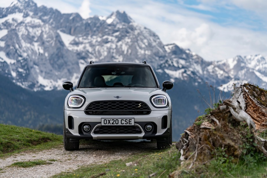 Front view of a white 2021 Mini Cooper Countryman subcompact SUV parked in front of snow-capped mountains on a partly sunny day