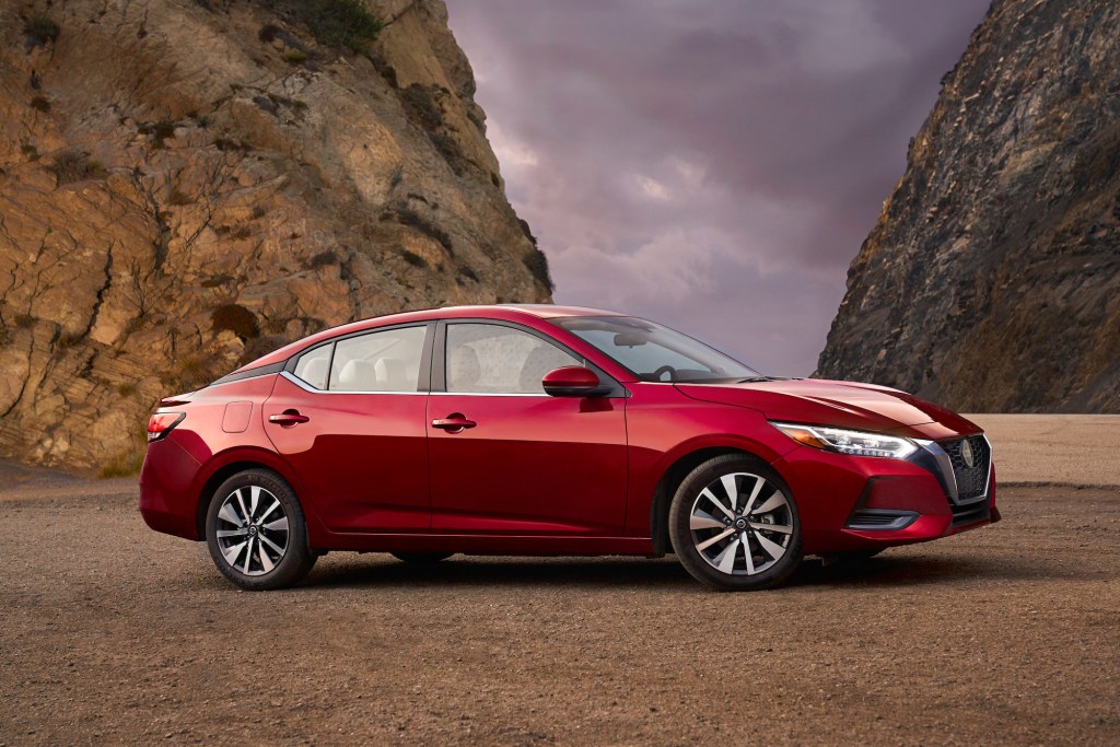 A red 2021 Nissan Sentra compact sedan parked between two mountains in front of dark clouds