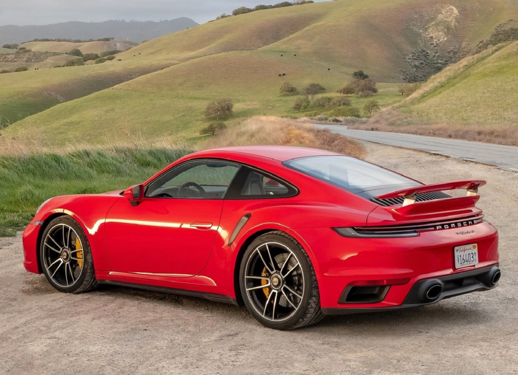 The rear 3/4 view of a red 2021 Porsche 911 Turbo S parked by a road through rolling green hills