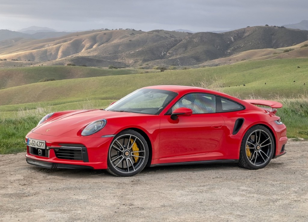 A red 2021 Porsche 911 Turbo S parked on a dirt parking space by rolling green hills