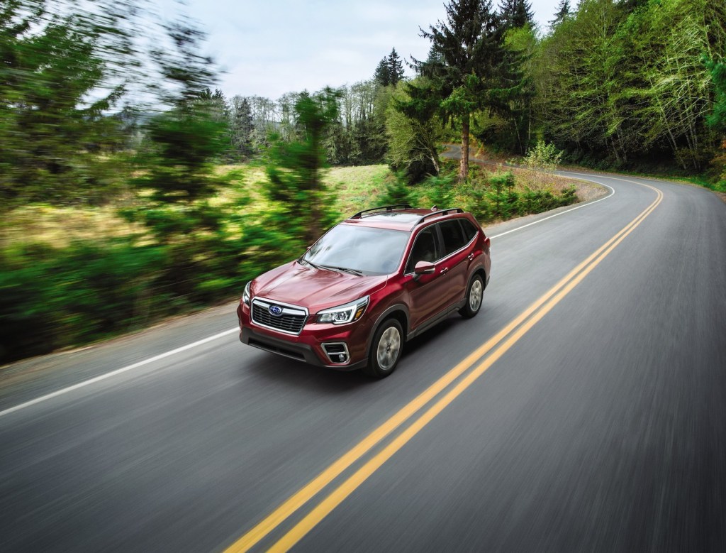A red 2021 Subaru Forester compact SUV driving down an empty tree-lined street