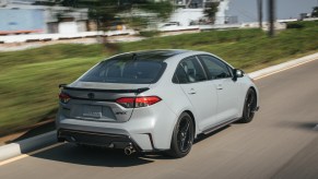 A light-gray 2021 Toyota Corolla Apex compact car travels on a road alongside a ship