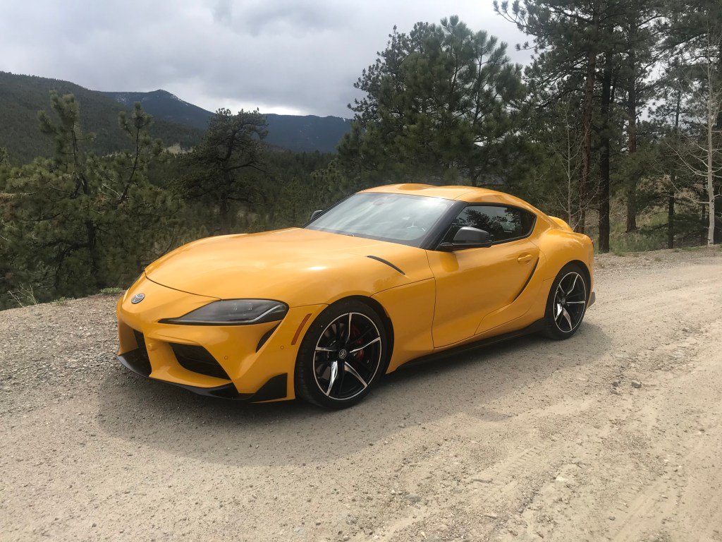 A yellow 2021 Toyota Supra 3.0 parked on a gravel spot on a tree-covered mountain