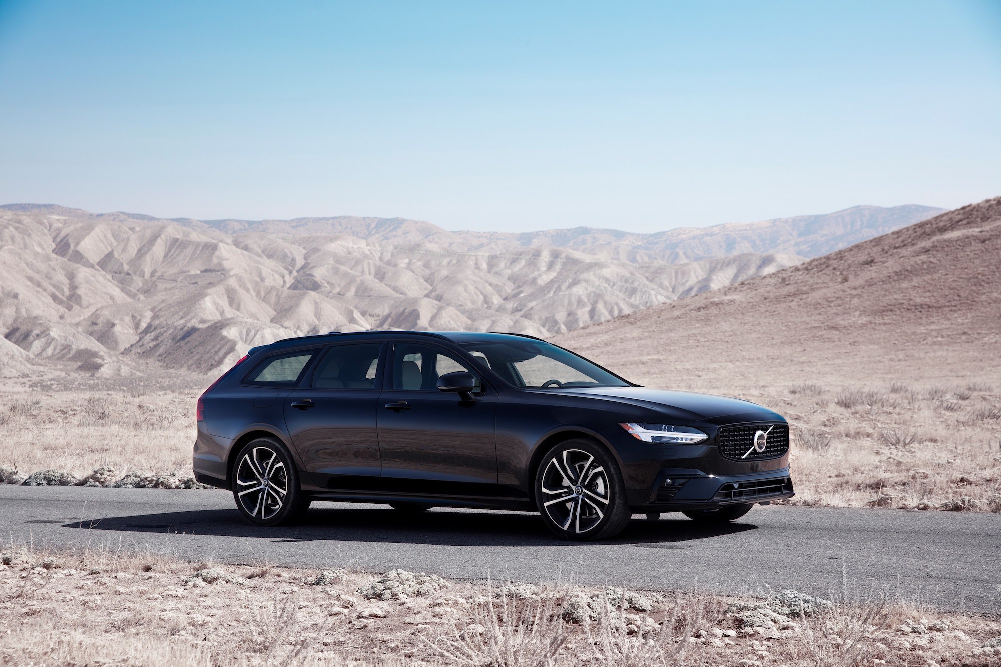 A black 2021 Volvo V90 station wagon parked on paved road through desert mountains