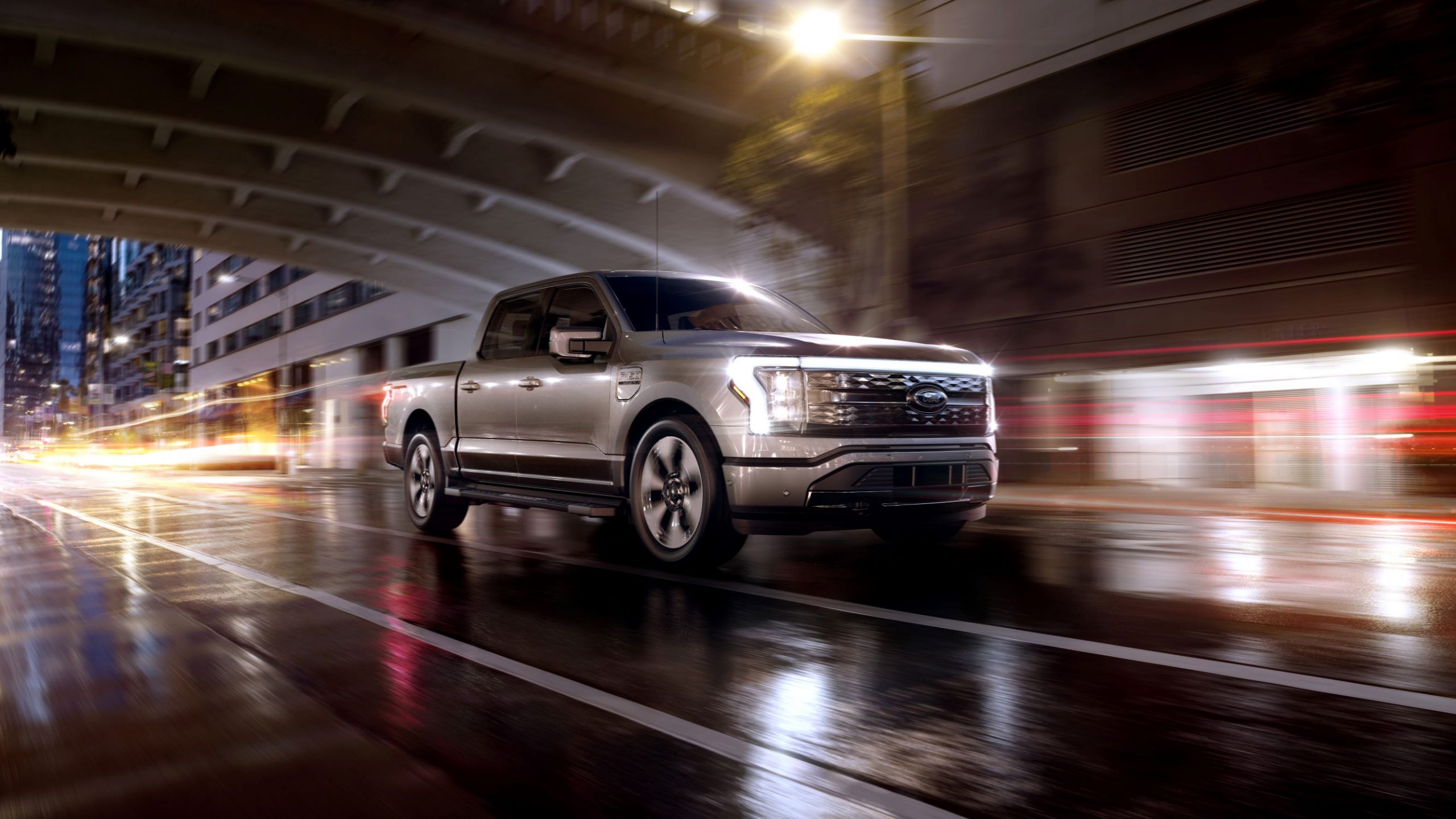 A silver 2022 Ford F-150 Lightning Platinum drives through a rain-soaked city at night