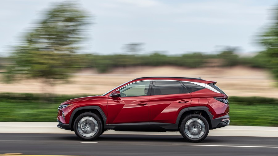 A red 2022 Hyundai Tucson travels on a highway along grass and trees. Hyundai and Kia are known for their generous car warranty coverage.