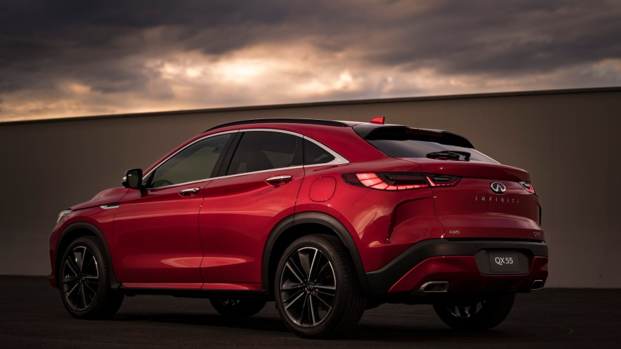 A red 2022 Infiniti QX55 AWD luxury compact crossover SUV parked next to a wall as dark clouds loom