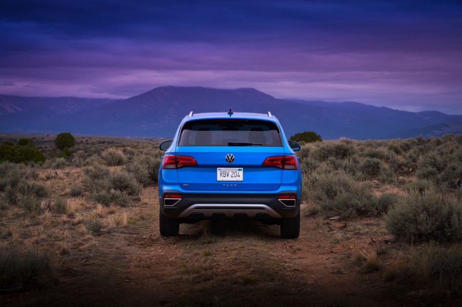 A rear view of a bright-blue 2022 Volkswagen Taos parked in a desert at dusk with mountains in the distance