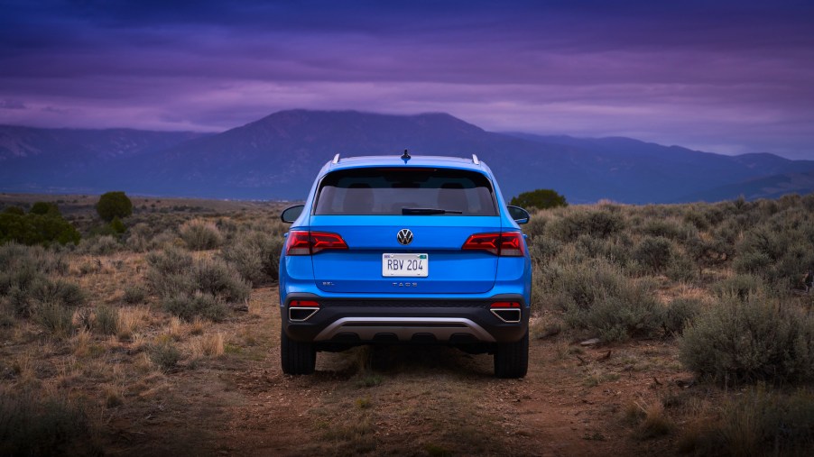 A rear view of a bright-blue 2022 Volkswagen Taos parked in a desert at dusk with mountains in the distance