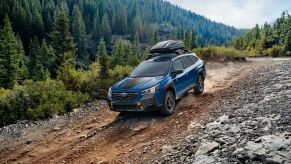 A blue 2022 Subaru Outback Wilderness driving down a dirt road near the forest