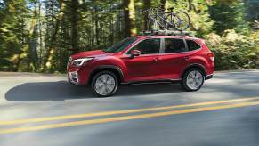 a red 2021 Subaru Forester driving on a scenic wooded road