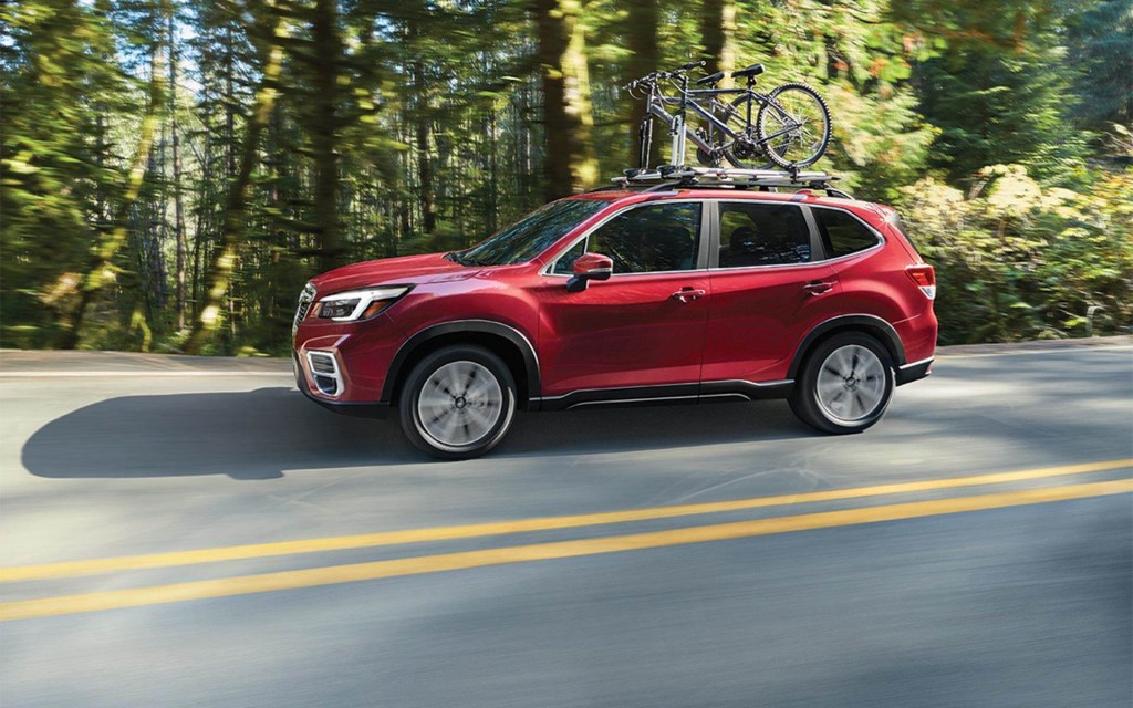 a red 2021 Subaru Forester crossover SUV driving on a scenic wooded road