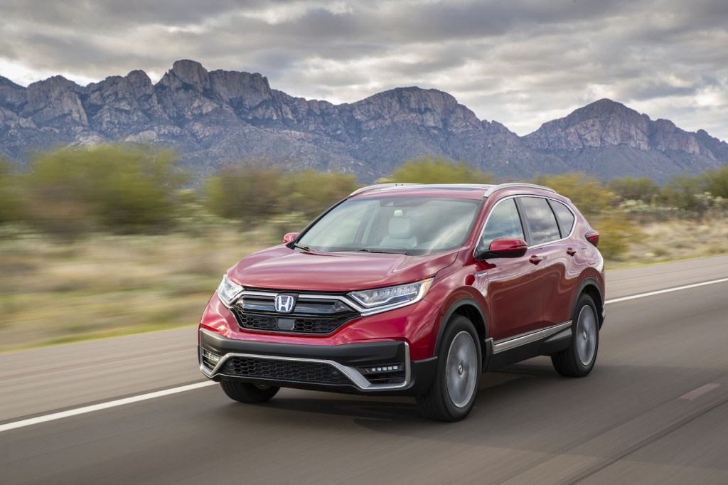 A red 2021 Honda CR-V Hybrid crossover SUV driving on a scenic highway near a mountain range