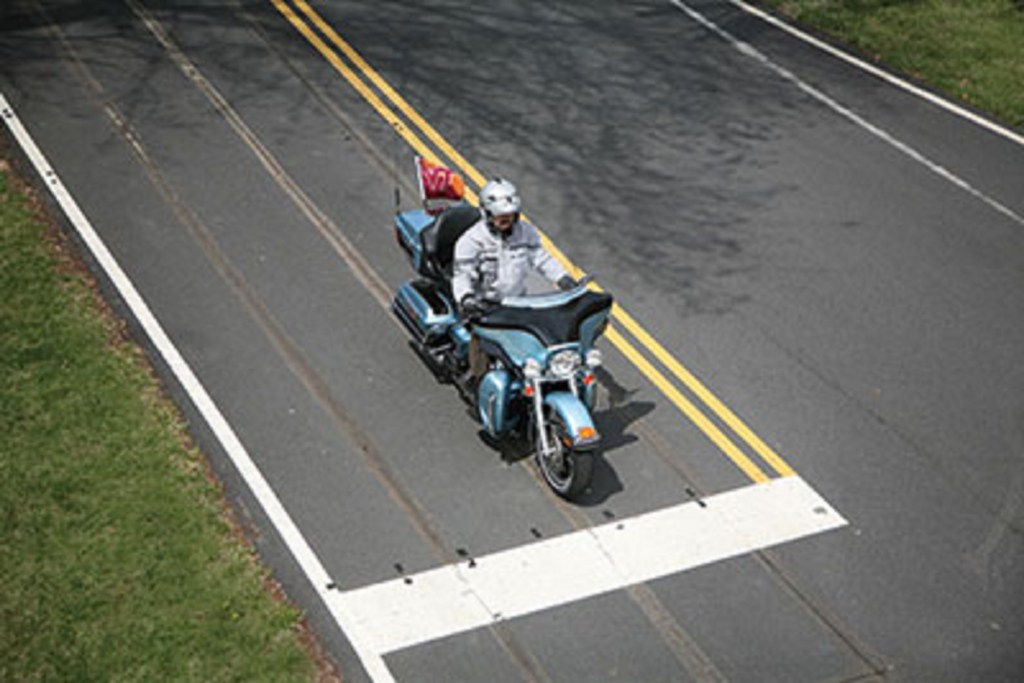 An FHWA engineer tests induction-loop traffic light sensor sensitivity on a light-blue motorcycle