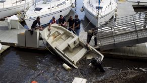 A group of people pull a Boston Whaler boat out of the water after it tipped over from a tsunami surge