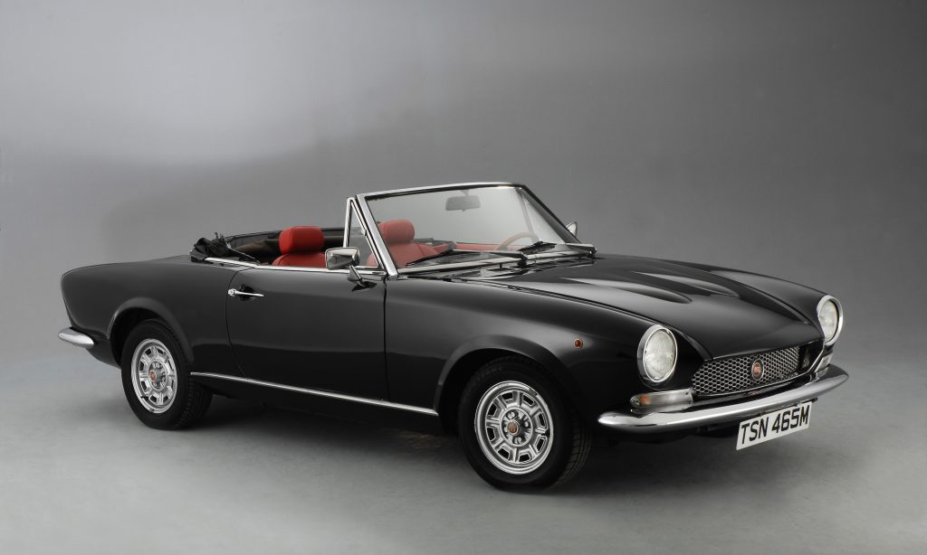 A black 1974 classic Fiat 124 Spyder convertible with red interior
