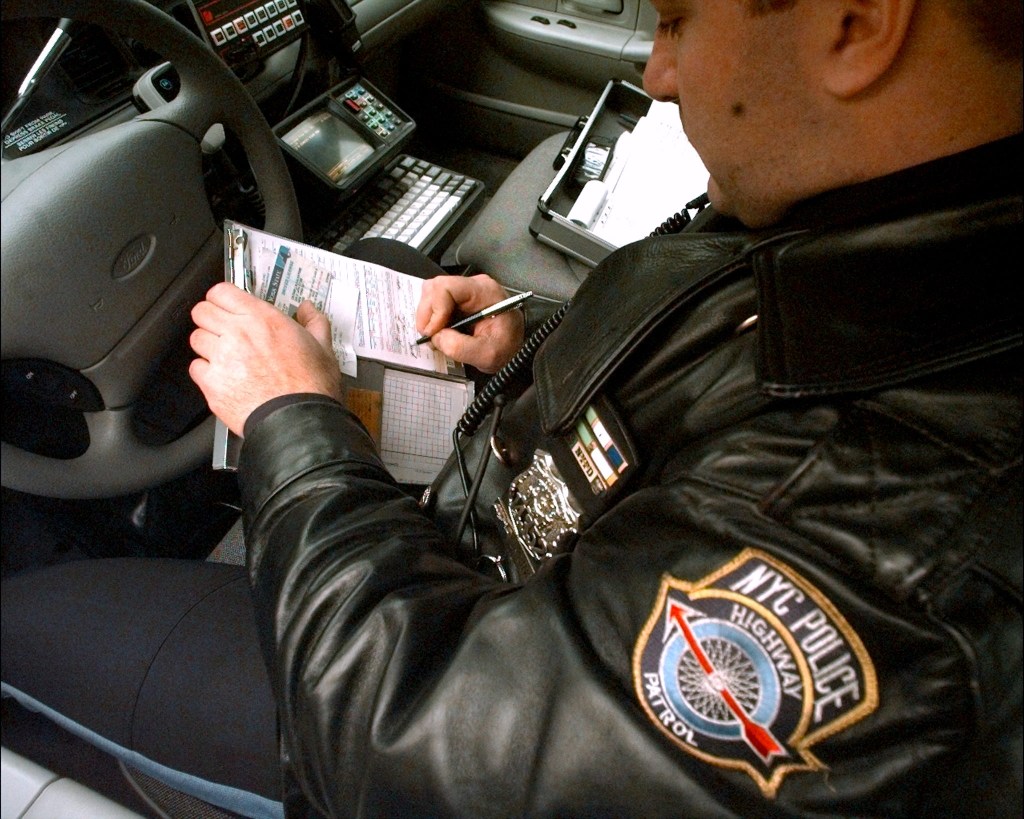 A police officer writes a speeding ticket after clocking cars with a radar gun. 