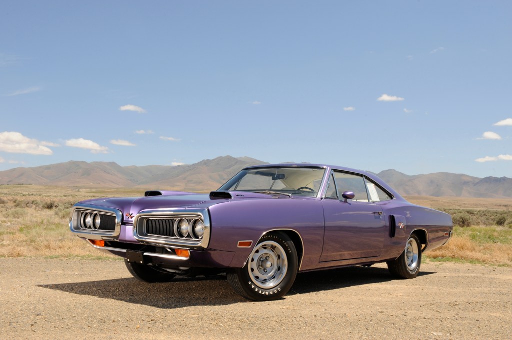 A 1970 purple Dodge Coronet Hemi RT sits on the dusty acrid planes, framed by mountains in the distance.
