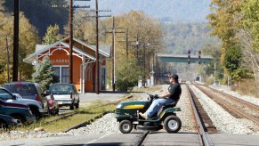A man driving a lawnmower in the street, in many areas lawnmower driving laws say mowers aren't street legal