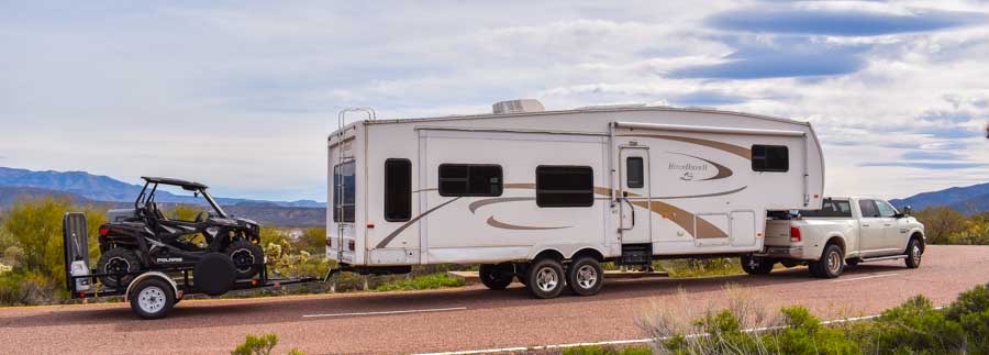 a truck towing an RV camper with a auto behind.