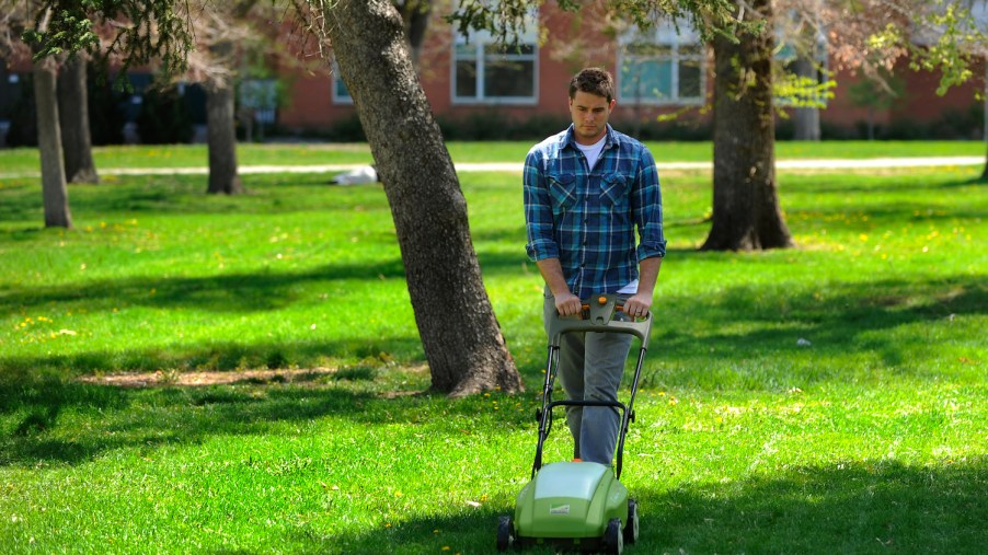 A young man demonstrating an electric lawn mower
