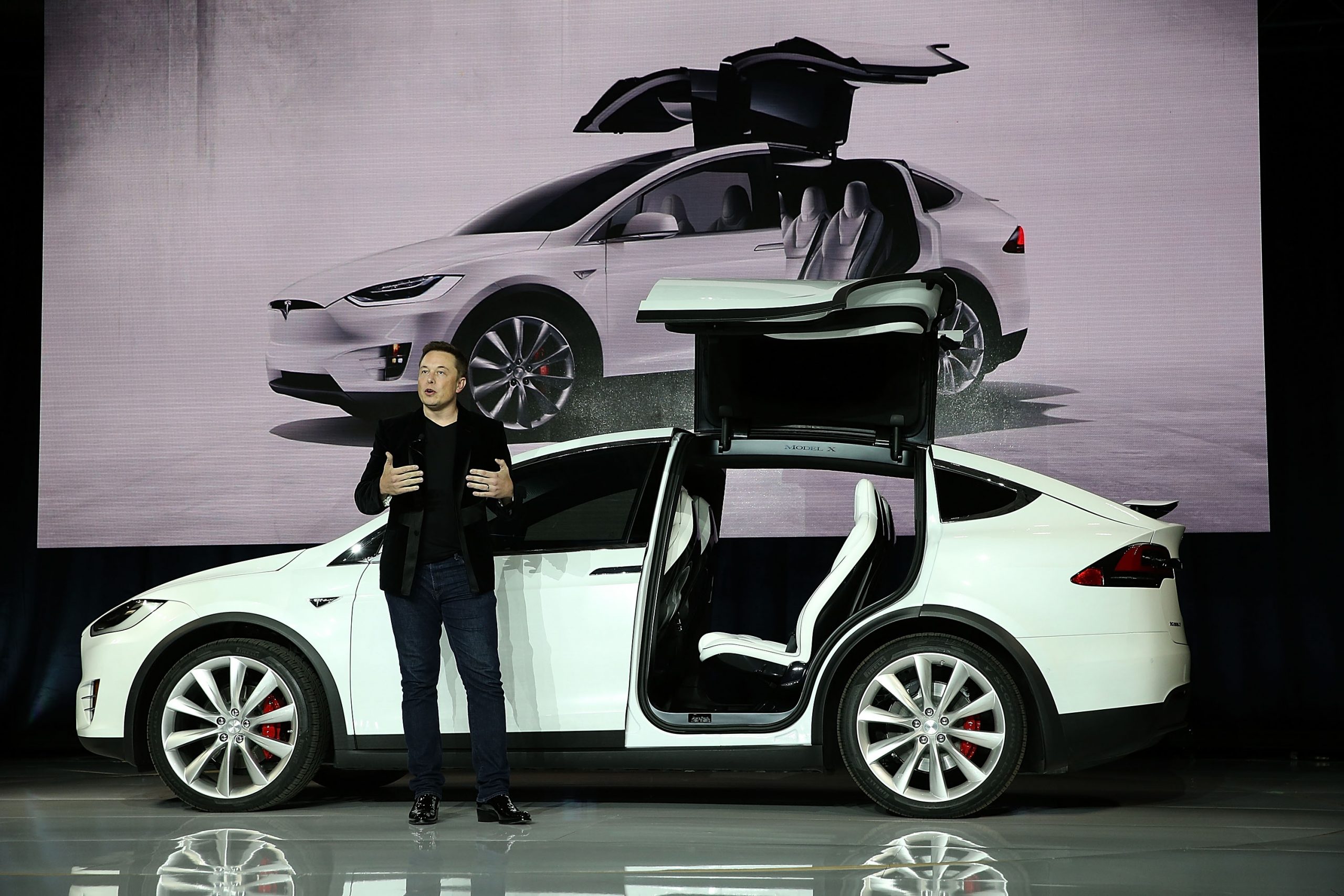 Elon Musk stands outside of a Tesla crossover vehicle.