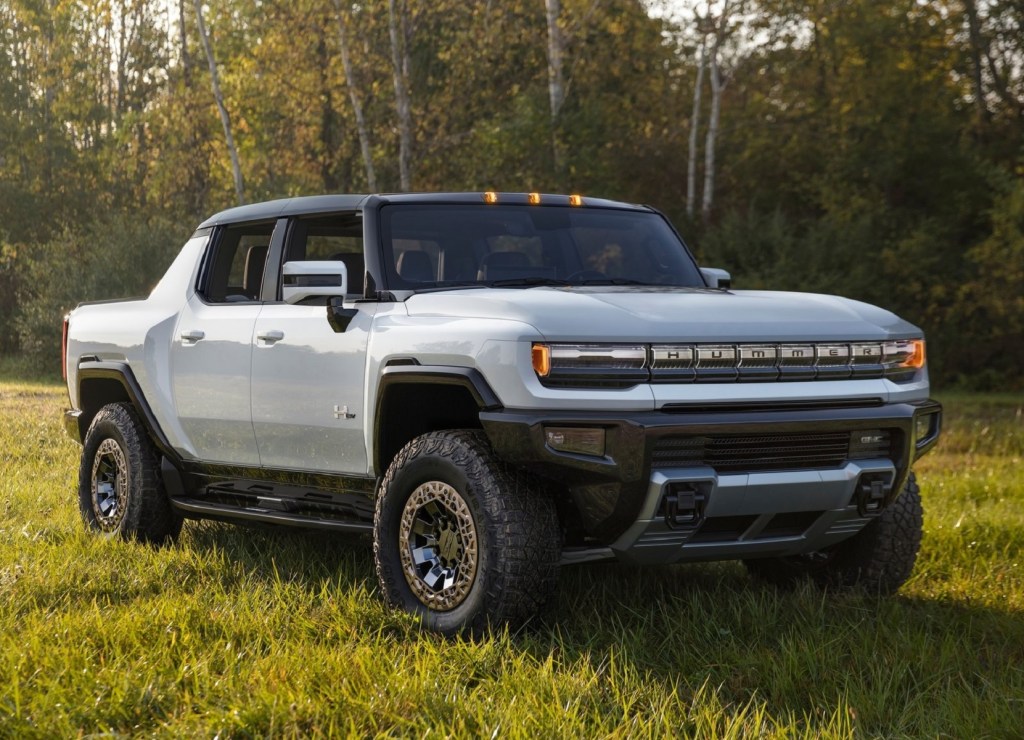 A white GMC Hummer EV Truck in a forest-lined grassy field
