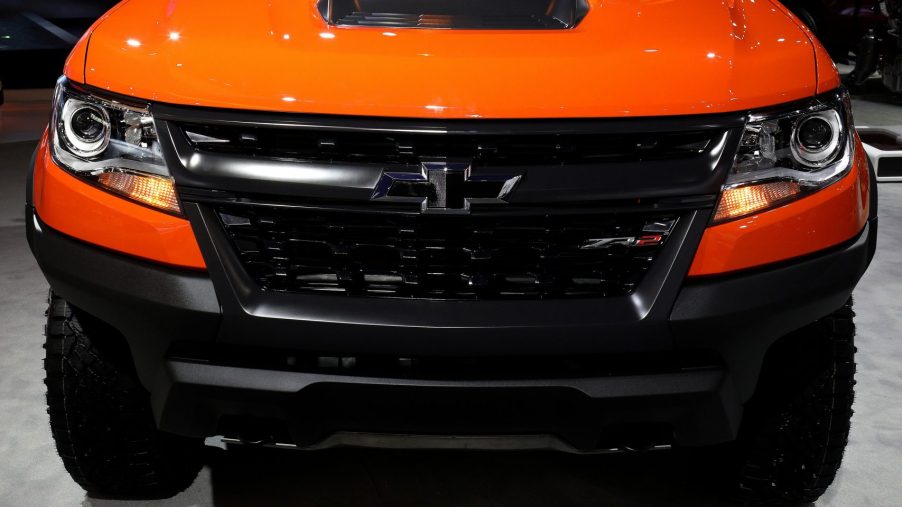 the front grille view of a bright orange Chevrolet Colorado on display at an auto show.