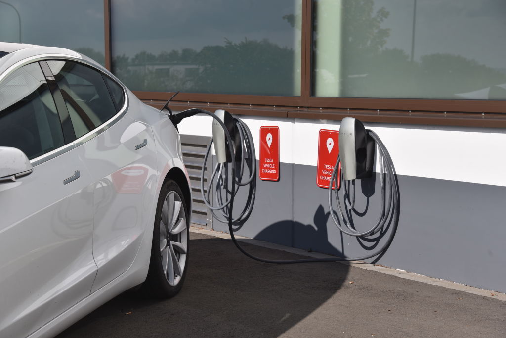 A white Tesla Model Y plugged into a charger outside