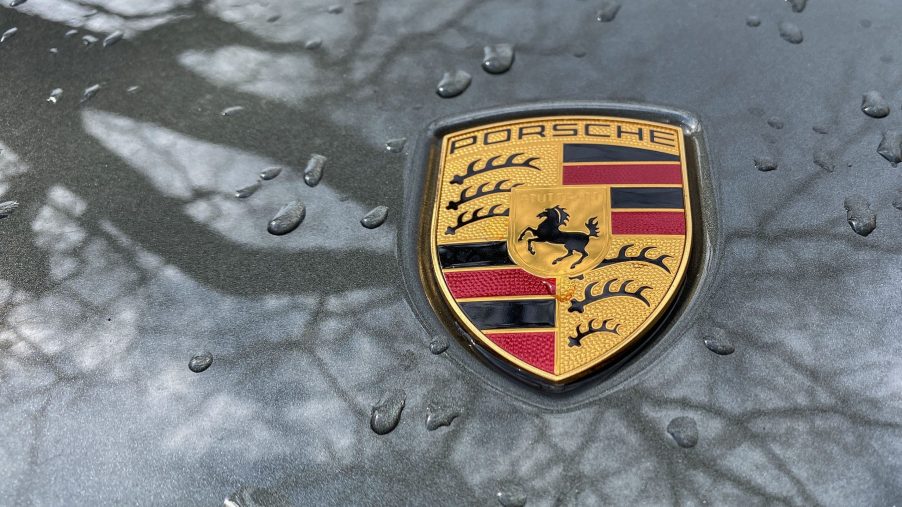 Porsche logo on a raindrop speckled car hood reflecting trees in the paint coat.