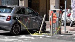 A silver Fiat 500 sits on a street plugged into an EV charger