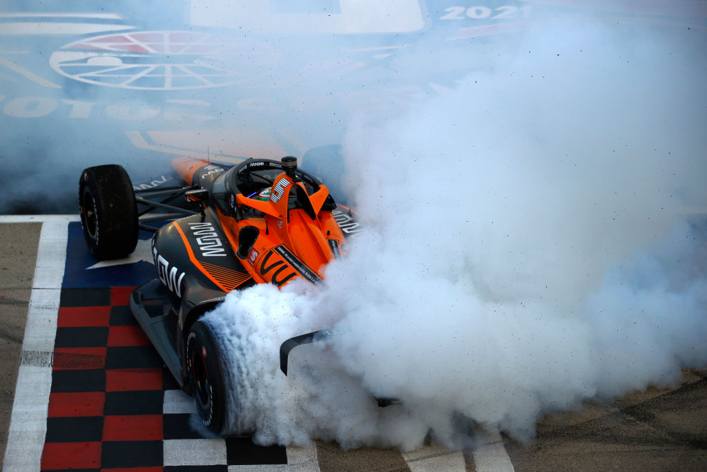An orange Mclaren Arrow Indy Car does a burnout.