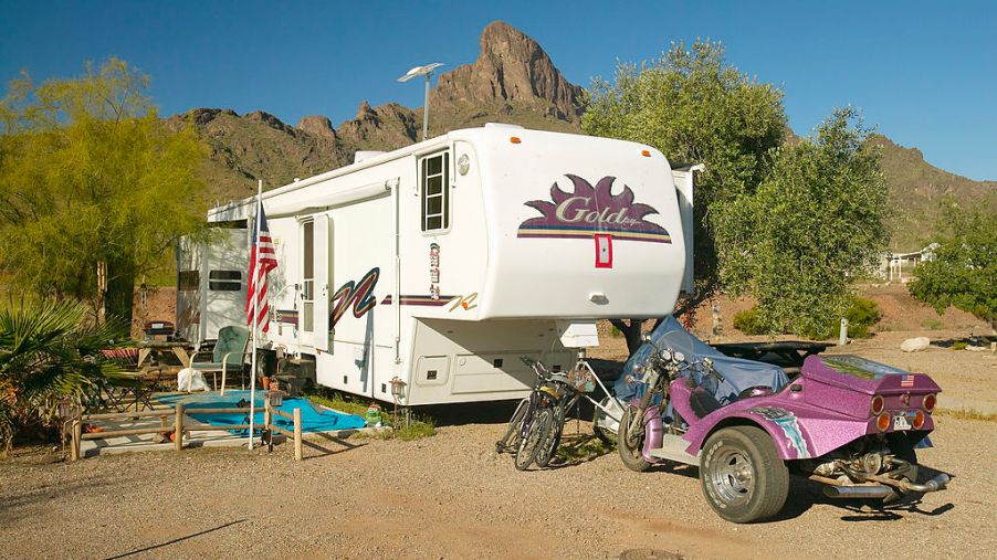 A camper RV traler unhitched at a campsite with bicycles and an off-road vehicle nearby.