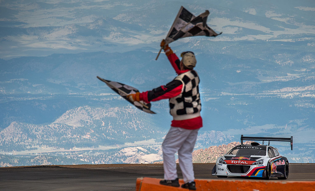A white and black hill climb car with a huge wing, driven by Sebastian Loeb crosses the line at Pikes Peak.