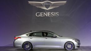 A silver Genesis sedan on stage with the Genesis logo in the background