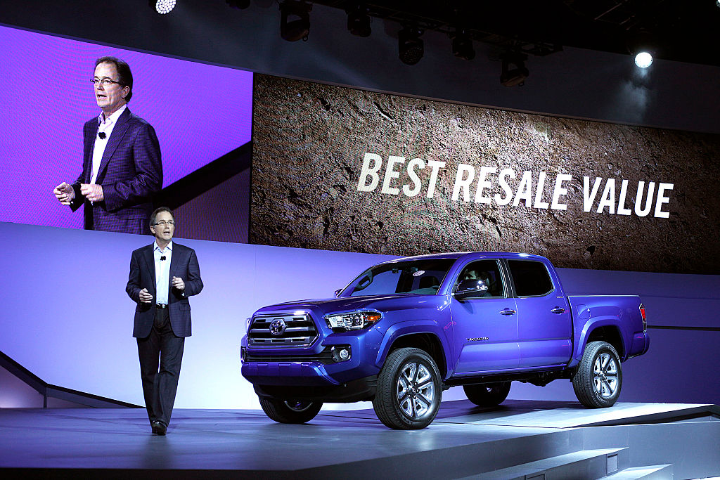 a blue Toyota Tacoma at an auto show on display with a best resale value banner in the background.