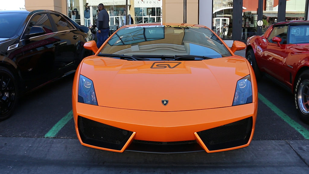 An orange Lamborghini Gallardo sits parked at a summer cars and coffee event 