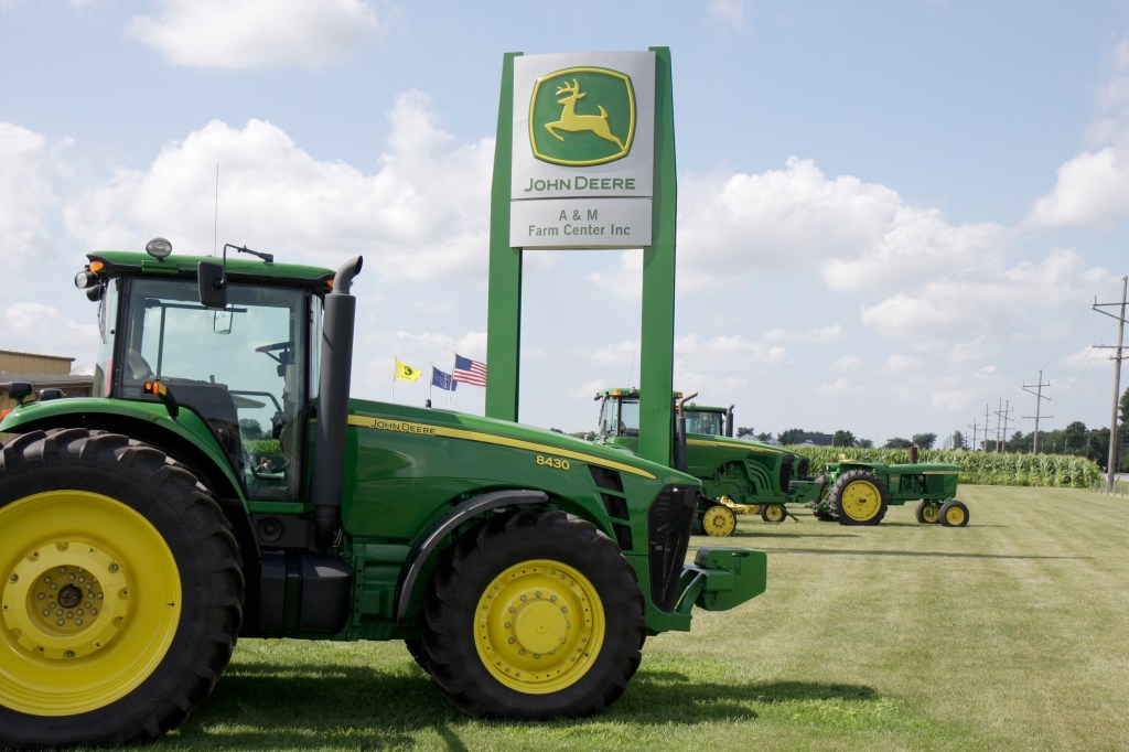 a John Deere tractor in front of a John Deere sign on a sunny day 