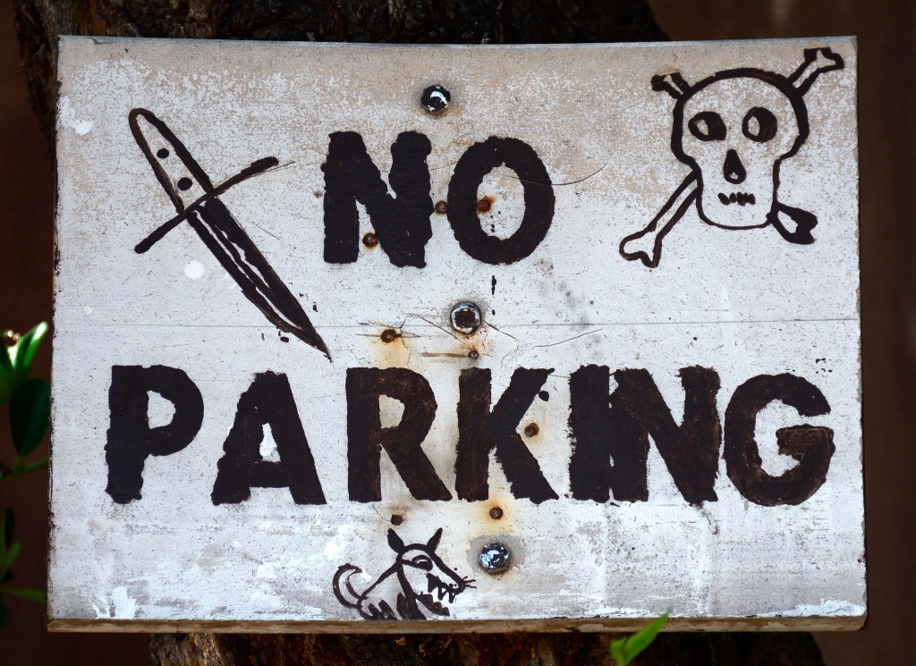 A 'No Parking' sign in Santa Fe, New Mexico, is embellished with threatening images including a skull-and-crossbones and a vicious dog.