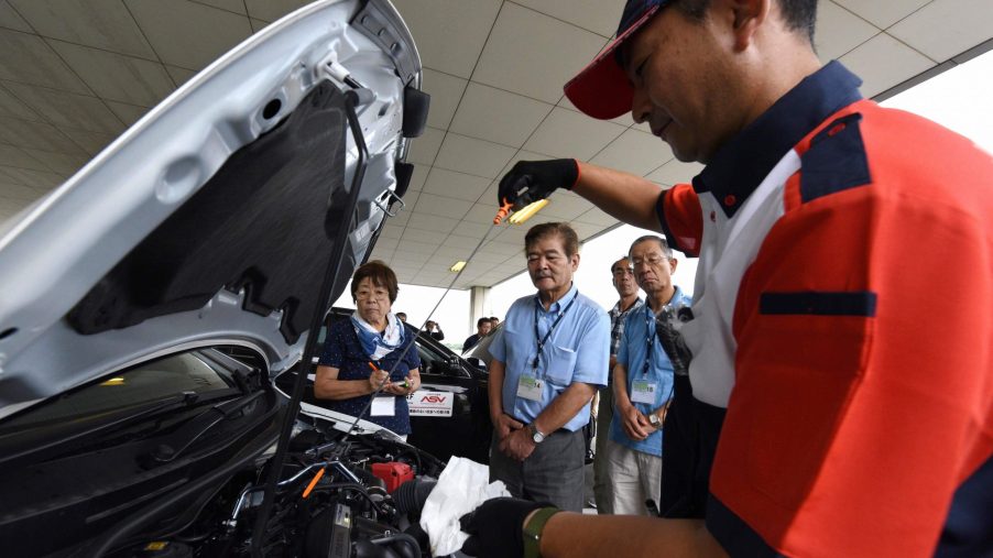 an instructor using a dipstick to check engine oil levels during a lesson on car maintenance at a driving school for senior citizens