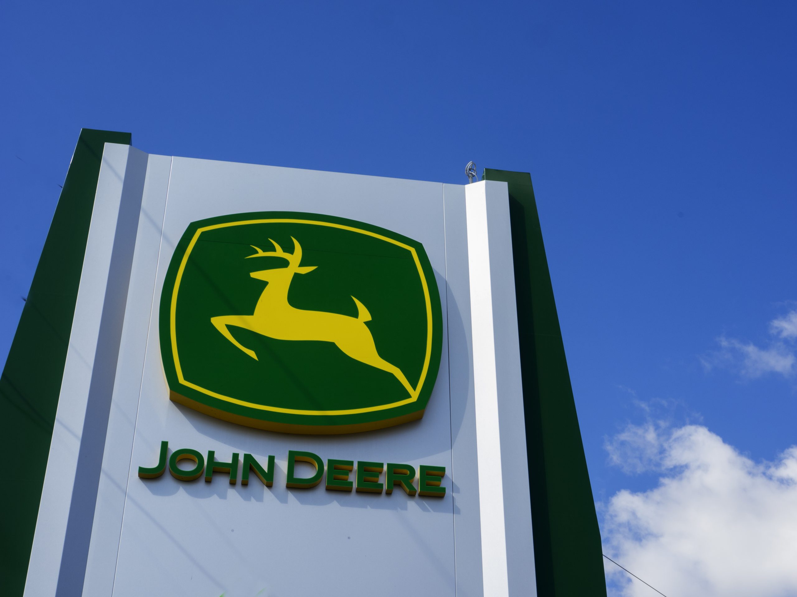 a John Deere logo on a tall sign with blue cloudy skies