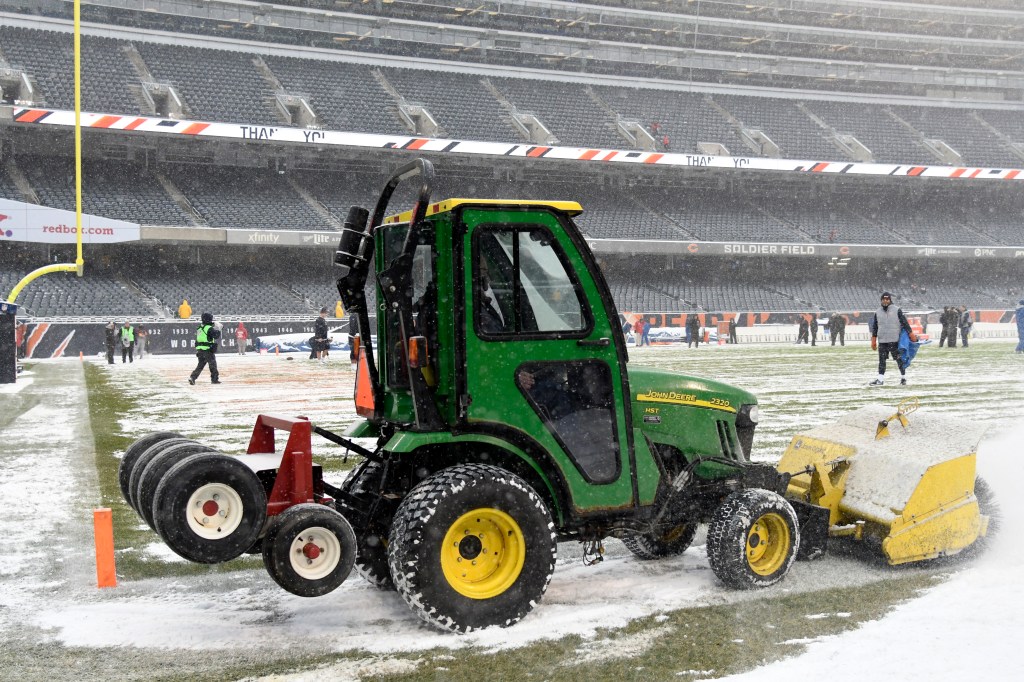 a John deer compact tractor plowing snow on a football field. 
