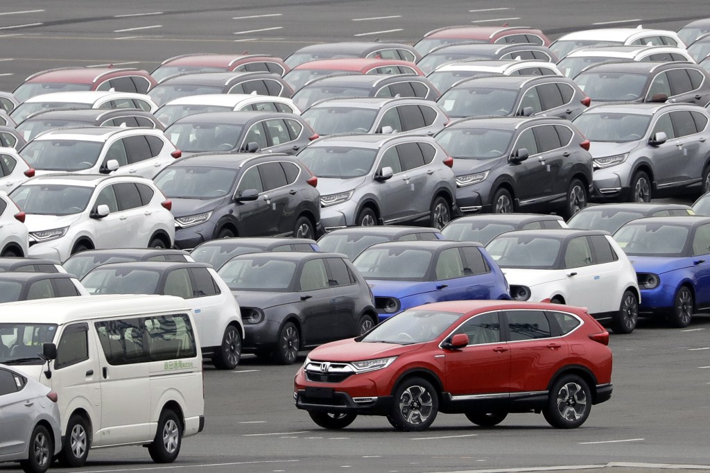 A red Honda Motor Co. CR-V sports utility vehicle (SUV) bound for shipment, bottom right, is driven while others sit parked at a port in Yokohama, Kanagawa Prefecture, Japan