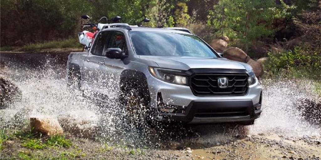 A silver 2021 Honda Ridgeline splashes through a puddle. Consumer Reports ratings for the Ridgeline are excellent.