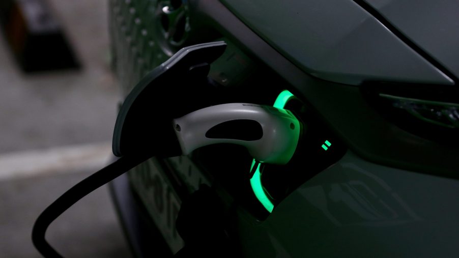 White Hyundai Kona EV SUV charging in a dark garage. The charging plug is lit in green.