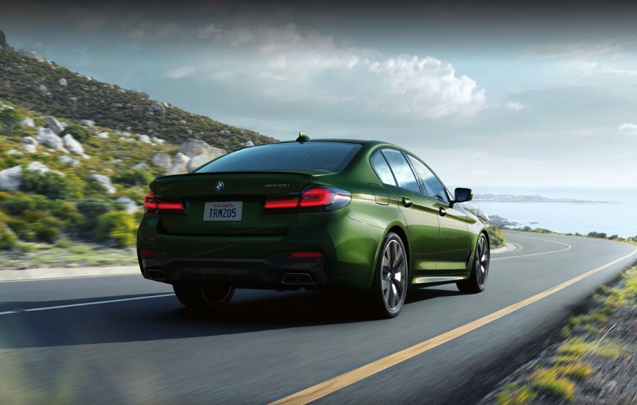 a bright green BMW 5 Series driving at speed on a scenic road near the sea
